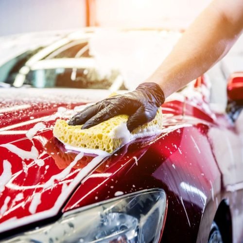 Worker washing red car with sponge on a car wash