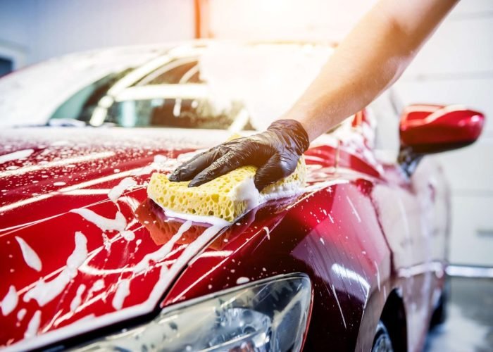 Worker washing red car with sponge on a car wash